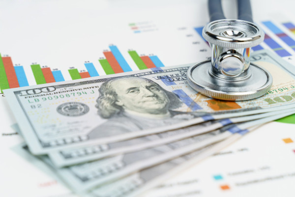 Stethoscope and money resting on graphs of data